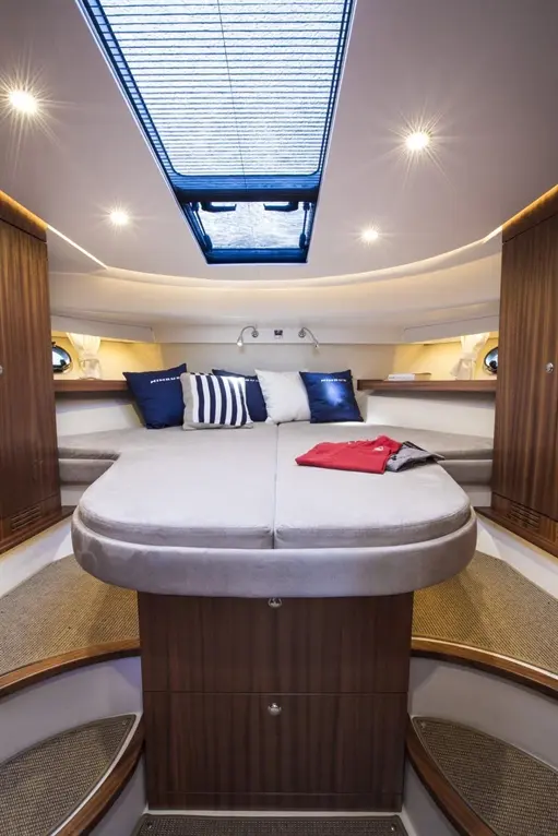 Spacious yacht interior featuring a double bed, blue and white pillows, and a red shirt on the bed, under a skylight.